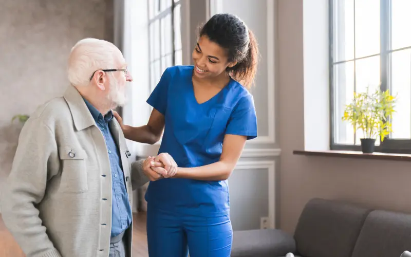 A nurse is helping an older man to put on his medical gloves.