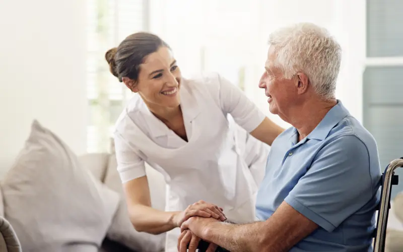 A nurse is holding the hand of an older man.